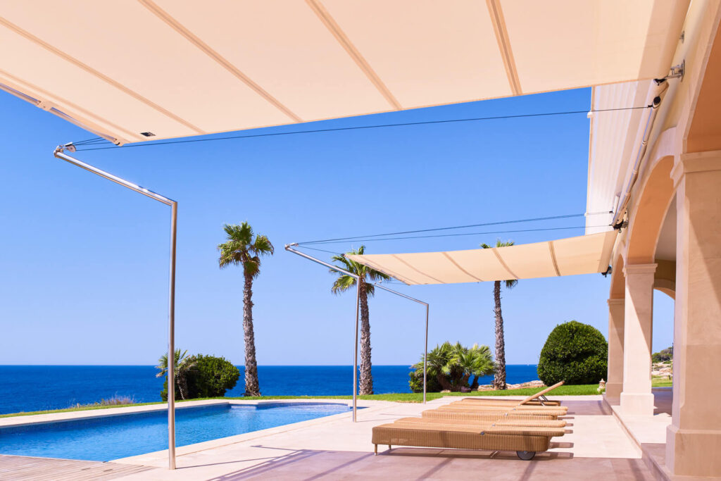 automatic sun sail deployed on Ibiza luxury villa terrace at golden hour, sea view and infinity pool beyond